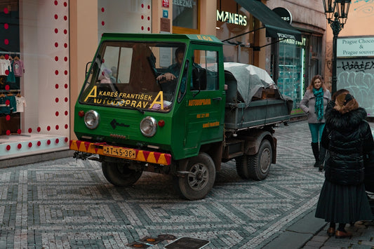 A small green truck parked on a cobblestone street.