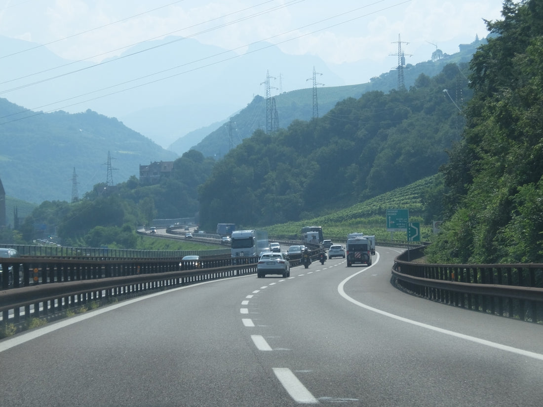 Cars and trucks drive on a highway through mountainous terrain.