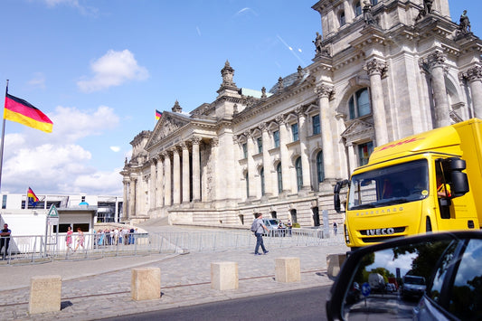 German flag flying near the reichstag building with vehicles.